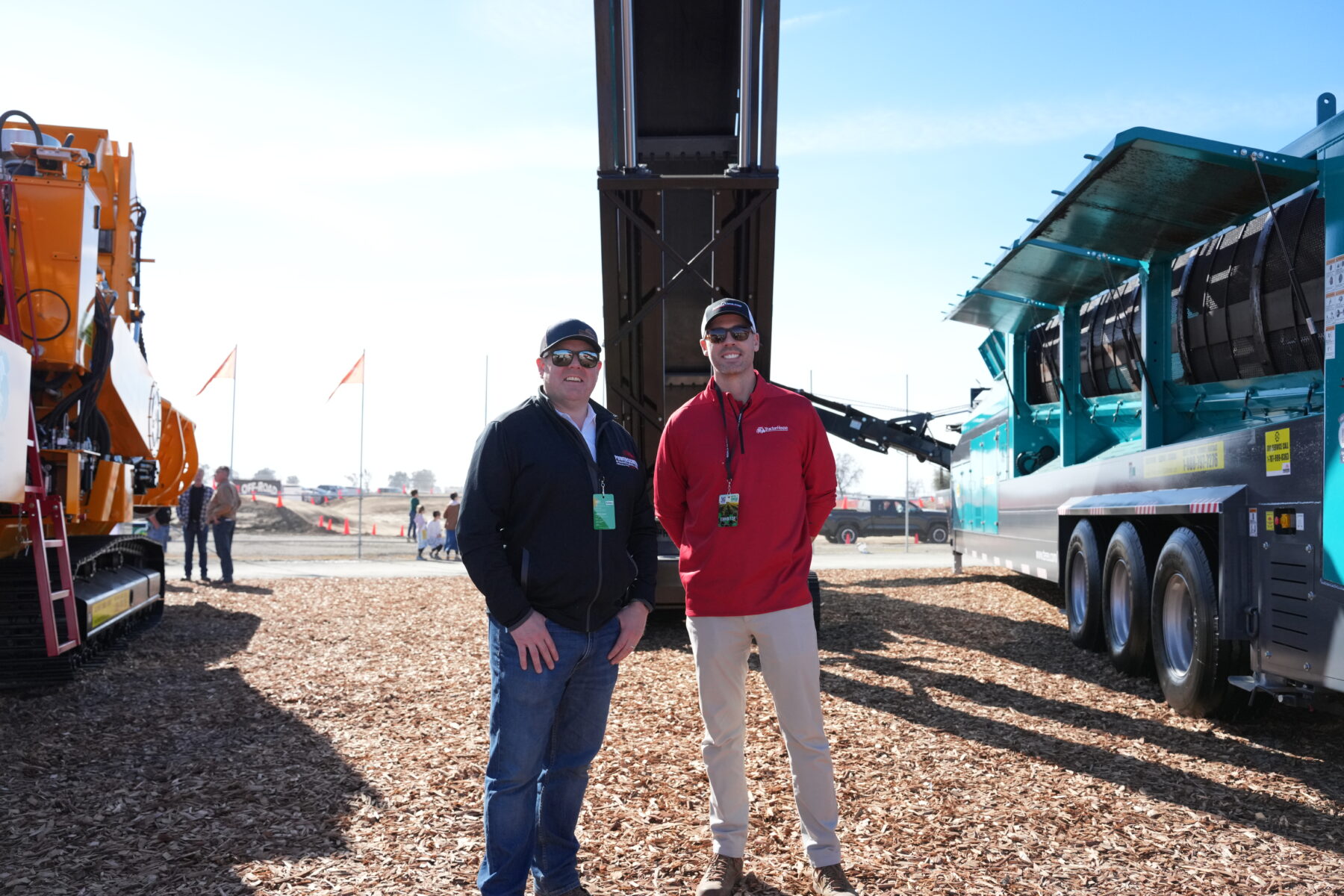 Two men smiling at camera while standing on bark in front of a conveyor