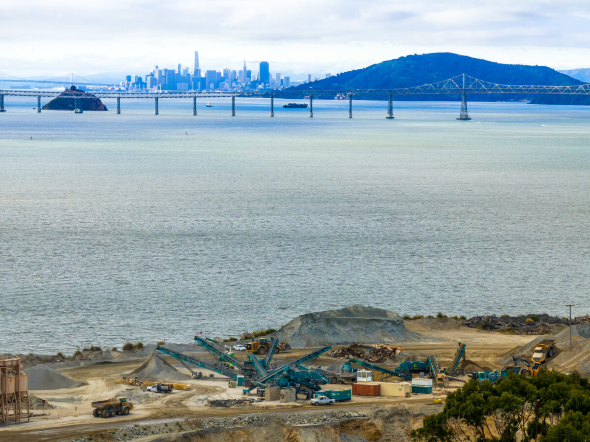 Cantera de roca cerca de la bahía de San Francisco con máquinas Powerscreen procesando áridos, con el horizonte de San Francisco y el puente de la bahía al fondo.