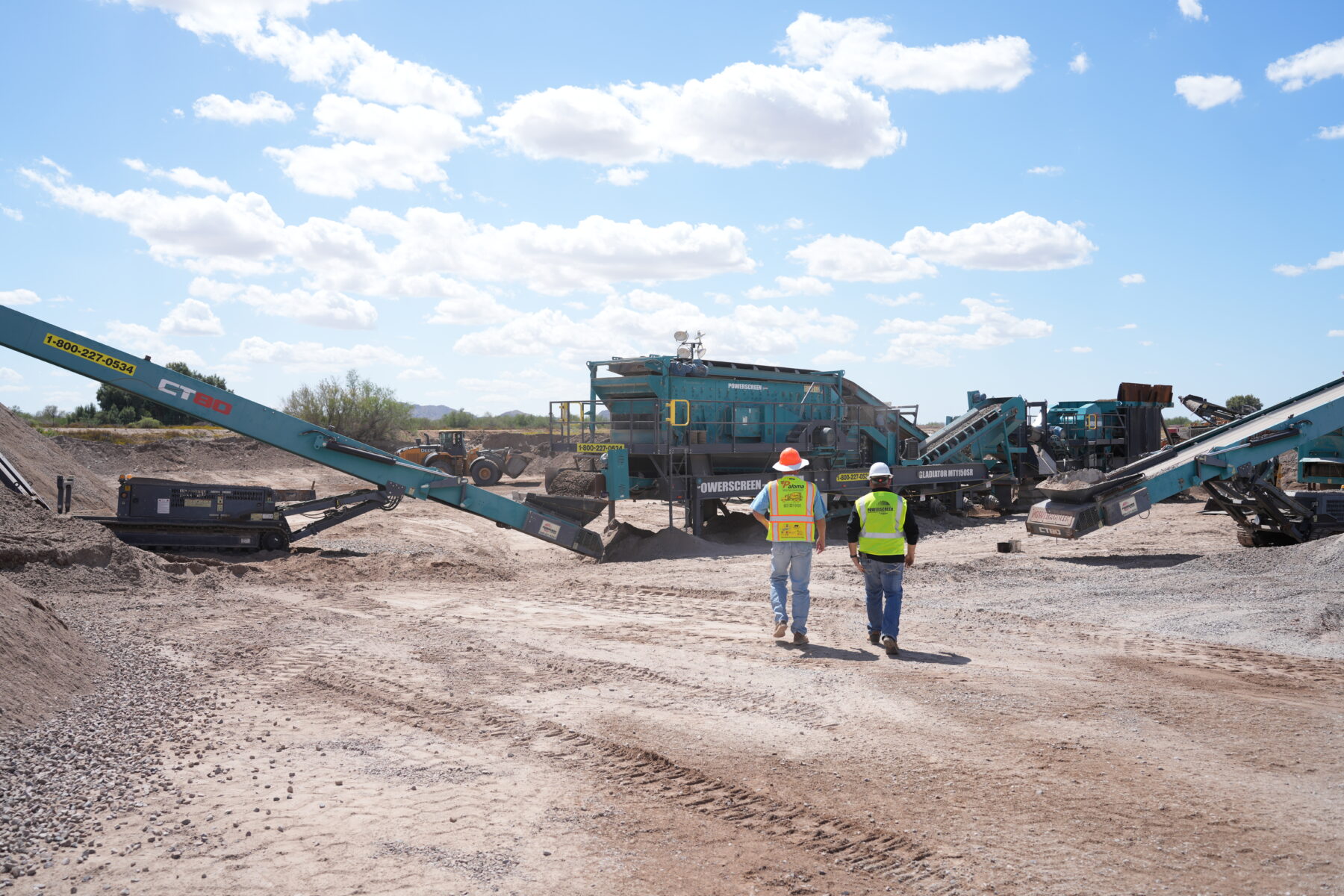 Two people in safety ppe walking toward a Powerscreen crushing and screening spread working