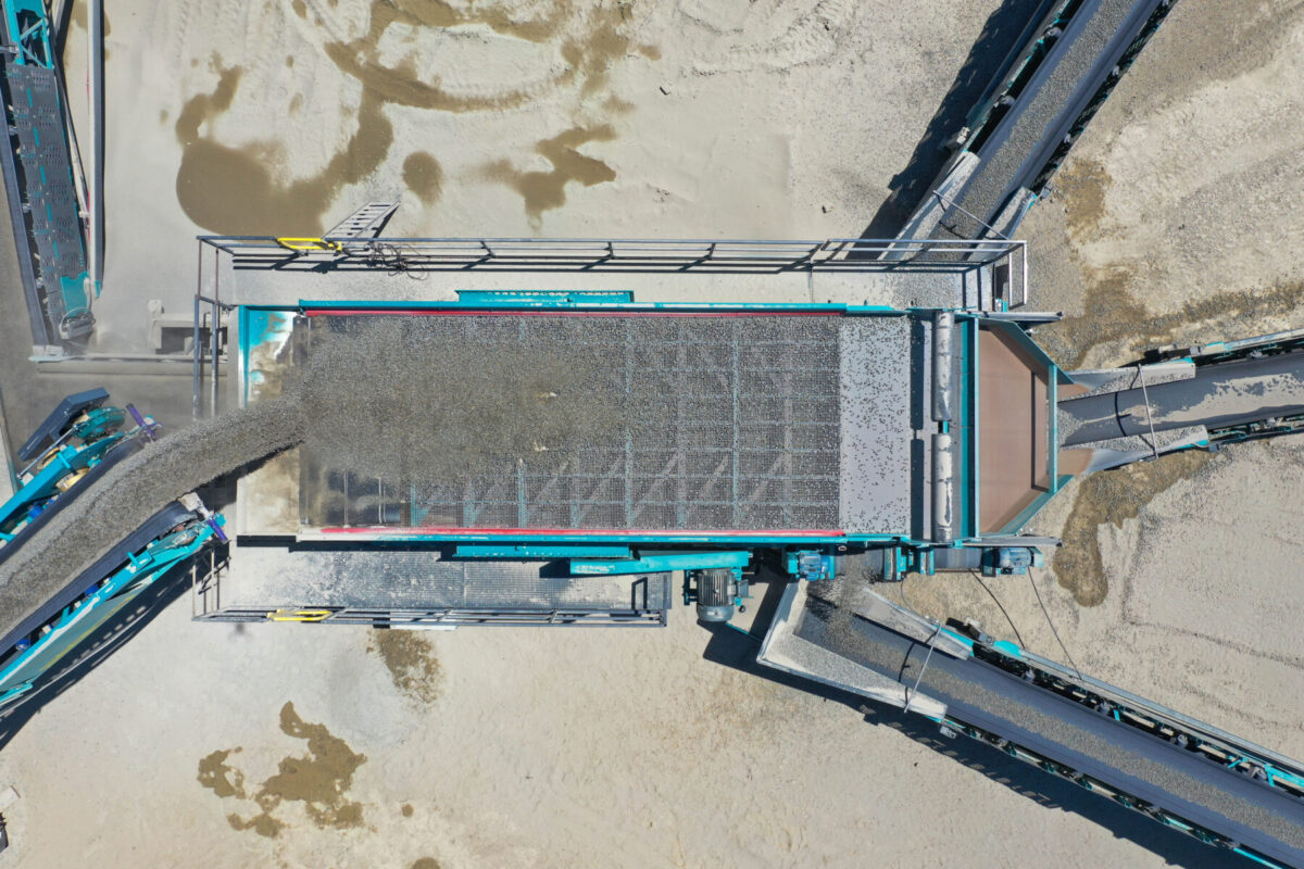 Vista aérea de una cribadora Powerscreen en acción, separando grava y áridos en distintos tamaños mediante varias cintas transportadoras.